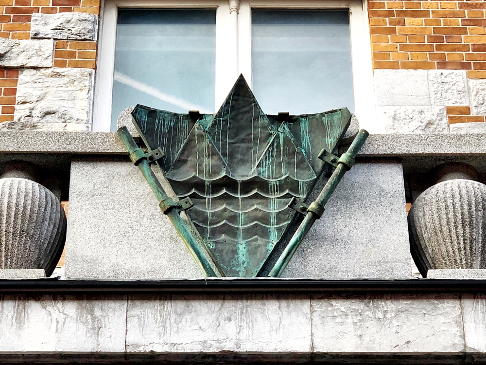 Plečnikov slovenski emblem nad glavnim vhodom Narodne in univerzitetne knjižnice v Ljubljani iz leta 1946, kamor je vključil vodo v obliki valovnic. Po prvotnem načrtu bi moral na tem mestu stati grb Kraljevine Jugoslavije. Foto: Aleksander Hribovšek, 2018.